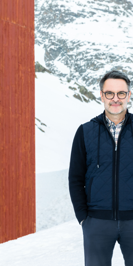 Giovanni Netzer steht neben dem markanten roten Turm auf dem verschneiten Julierpass, vor der eindrucksvollen Kulisse der Bündner Berge.