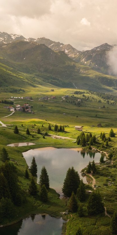 Morgenstimmung auf der Alp Flix mit kleinen Bergseen, saftigen Wiesen und dichten Arvenwäldern unter tief hängenden Wolken und Gipfeln.