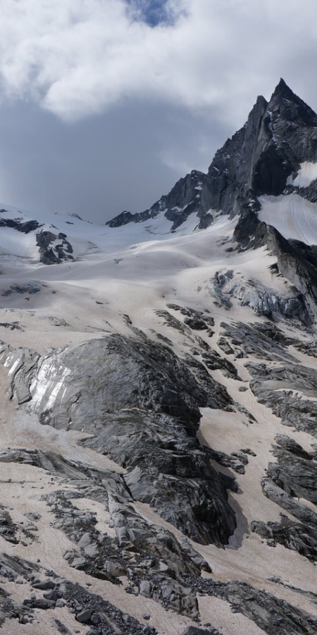 Ein zurückweichender Gletscher in Graubünden zieht sich zwischen schroffen, dunklen Felswänden und schneebedeckten Gipfeln hindurch.