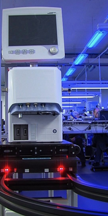 Modernes Labor in blauem Licht mit automatisierten technischen Geräten, Arbeitsstationen und Mitarbeitenden in einer industriellen Forschungsumgebung.