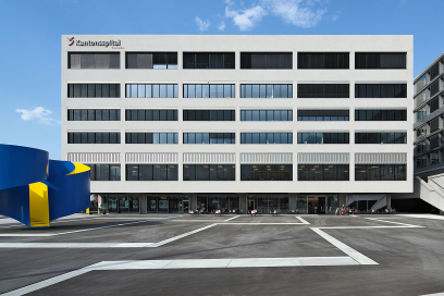 Modernes Hauptgebäude des Kantonsspitals Graubünden mit heller Fassade, grossen Fensterreihen und blau-gelber Skulptur auf dem Vorplatz.