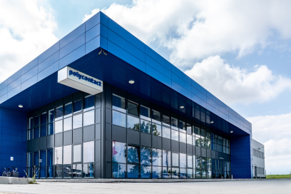 Modernes Firmengebäude von Polycontact mit blauer Metallfassade, grossen Fensterfronten und markantem Eingangsbereich unter leicht bewölktem Himmel.