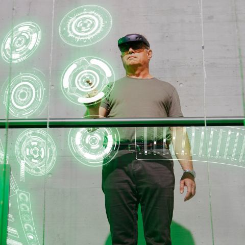 Mann nutzt eine Mixed-Reality-Brille und interagiert mit virtuellen Bedienelementen in einer modernen Arbeitsumgebung.