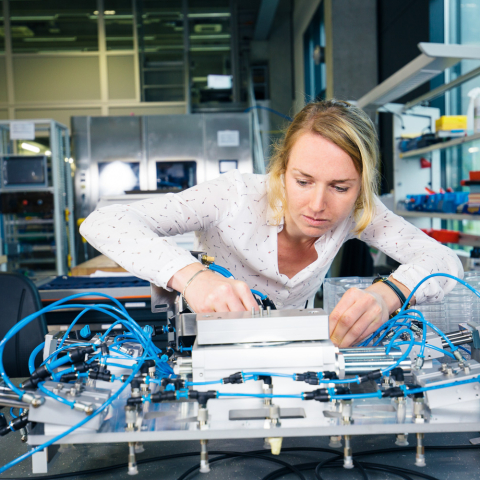 Mitarbeiterin arbeitet konzentriert an einer elektronischen Anlage mit Pneumatik und Sensorik in einem modernen Entwicklungslabor.