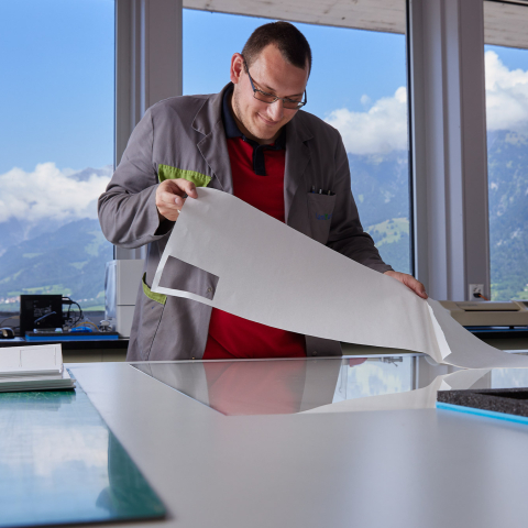 Ein Mitarbeiter bei LandQart prüft einen grossen Papierbogen in einem hellen Arbeitsraum mit Blick auf die Bündner Berglandschaft.