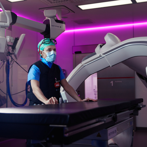 Eine medizinische Fachperson des Kantonsspitals Graubünden bedient moderne Bildgebungsgeräte in einem violett beleuchteten Operationssaal.