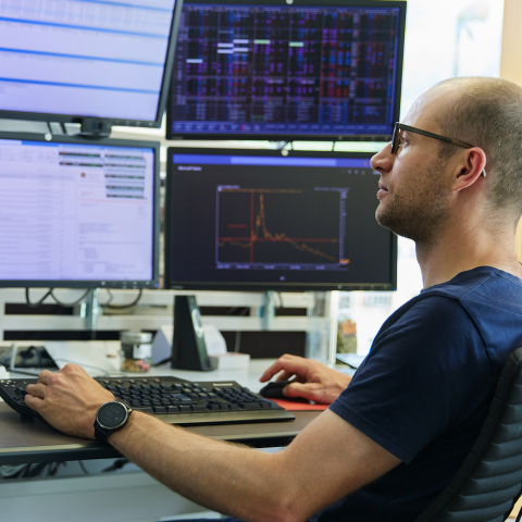 Repower-Mitarbeiter überwacht Energiedaten an Kontrollzentrum mit mehreren Bildschirmen, Tastatur und Telefon auf Schreibtisch, technisches Monitoring-System.