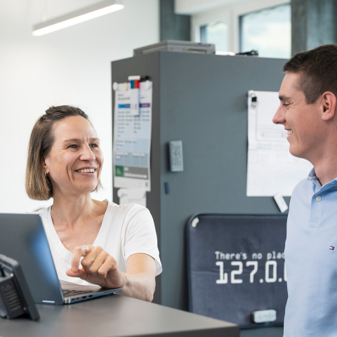 Drei Mitarbeitende bei INTEGRA unterhalten sich lächelnd an einem Stehpult mit Laptop in einem hellen, modernen Büro.