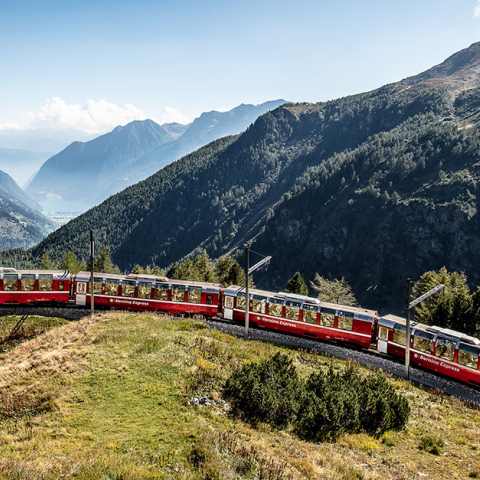 Der rote Bernina Express der Rhätischen Bahn fährt mit seinen Panoramawagen durch eine weitläufige alpine Berglandschaft.