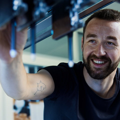 Ein lächelnder Mitarbeiter von HamiltonInfo montiert in einer modernen Werkhalle präzise Bauteile an einer technischen Anlage.