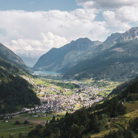 Weitblick über das Puschlav in der Region Bernina mit dem Dorf Poschiavo, grünen Wiesen, bewaldeten Hängen und markanten Bergketten.