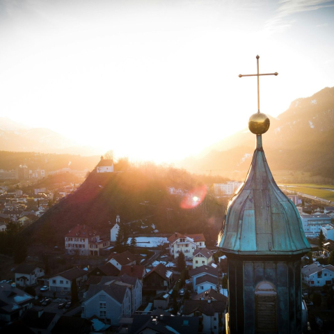 Panorama der Region Imboden bei Sonnenuntergang mit Kirchturm im Vordergrund, Ortschaft und Bergen im warmen Abendlicht.