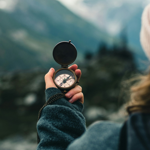 Eine Person hält vor einer unscharfen Bündner Berglandschaft einen Kompass in der Hand und steht sinnbildlich für das Entdecken Graubündens.