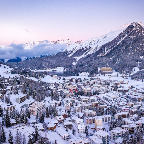 Verschneites Panorama von Davos mit dem lebendigen Alpenort, umgeben von bewaldeten Hängen, weiten Skipisten und hohen Gipfeln.
