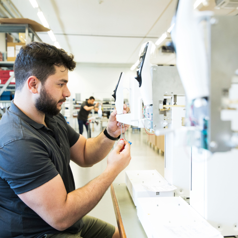 Ein Mitarbeiter bei INTEGRA Biosciences montiert Kabel und elektronische Komponenten an einem Laborgerät in einer hellen Produktionshalle.