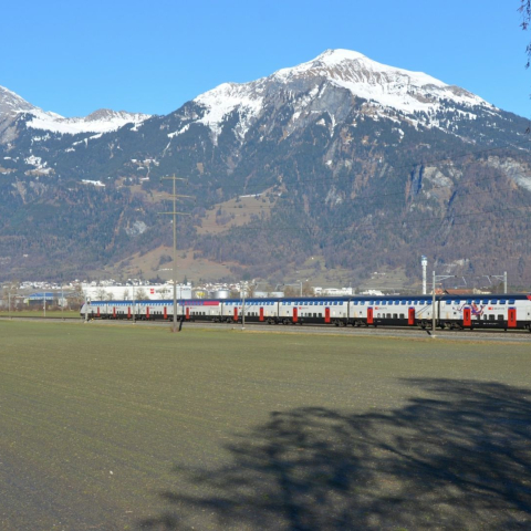 Ein SBB-Zug fährt durch die offene Landschaft bei Landquart, vor dem Panorama der verschneiten Bündner Berge und bewaldeten Hänge.