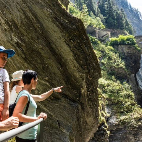 Eine Familie bestaunt von einem Steg aus die tief eingeschnittene Viamala-Schlucht mit steilen Felswänden, Wasserfall und historischen Brücken.