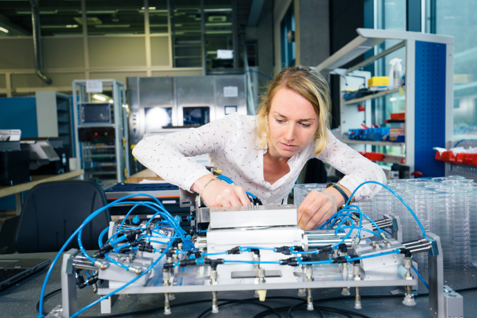 Mitarbeiterin arbeitet konzentriert an einer elektronischen Anlage mit Pneumatik und Sensorik in einem modernen Entwicklungslabor.