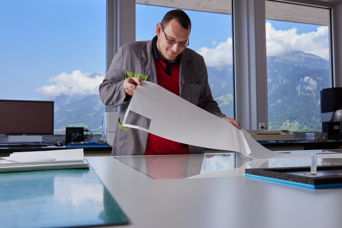 Ein Mitarbeiter bei LandQart prüft einen grossen Papierbogen in einem hellen Arbeitsraum mit Blick auf die Bündner Berglandschaft.