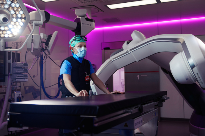 Eine medizinische Fachperson des Kantonsspitals Graubünden bedient moderne Bildgebungsgeräte in einem violett beleuchteten Operationssaal.