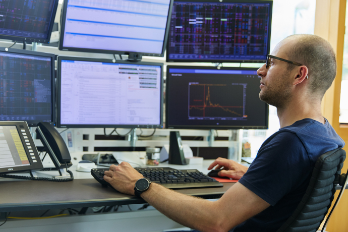 Repower-Mitarbeiter überwacht Energiedaten an Kontrollzentrum mit mehreren Bildschirmen, Tastatur und Telefon auf Schreibtisch, technisches Monitoring-System.