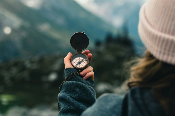 Eine Person hält vor einer unscharfen Bündner Berglandschaft einen Kompass in der Hand und steht sinnbildlich für das Entdecken Graubündens.