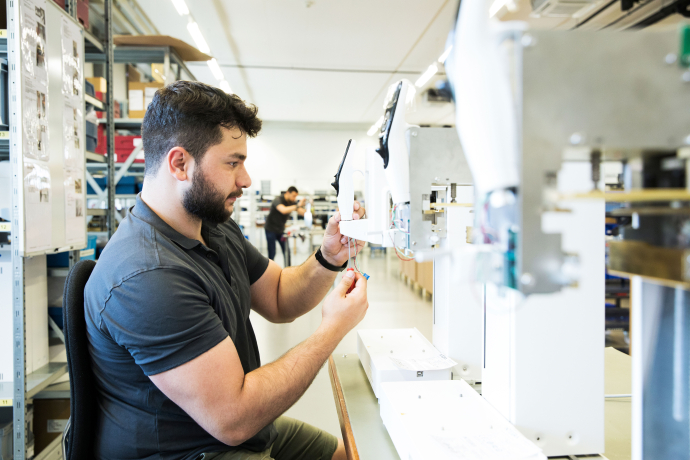 Ein Mitarbeiter bei INTEGRA Biosciences montiert Kabel und elektronische Komponenten an einem Laborgerät in einer hellen Produktionshalle.