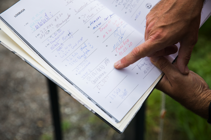 Eine Person bei LandQart zeigt auf handschriftliche Einträge und Berechnungen in einem aufgeschlagenen Logbuch im Freien.