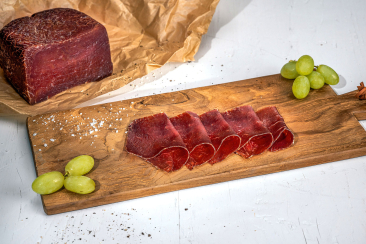 Dünn geschnittenes Bündnerfleisch auf einem rustikalen Holzplättli, angerichtet mit grünen Trauben, Salz und einem ganzen Fleischstück.