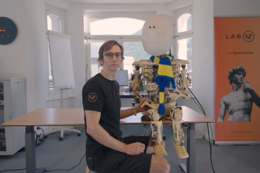Ein Entwickler sitzt im Labor von Lab42 neben einem humanoiden Roboter und zeigt, wie künstliche Intelligenz in Graubünden Gestalt annimmt.