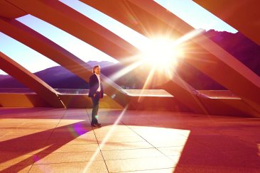 Eine Frau steht im Abendlicht unter der markanten Holzkonstruktion des Valerio-Olgiati-Baus in Sils, mit Blick auf die Engadiner Bergwelt.