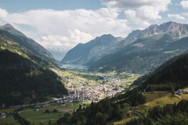 Weitblick über das Puschlav in der Region Bernina mit dem Dorf Poschiavo, grünen Wiesen, bewaldeten Hängen und markanten Bergketten.