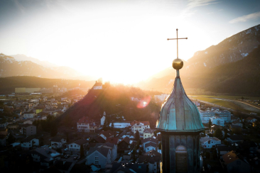 Panorama der Region Imboden bei Sonnenuntergang mit Kirchturm im Vordergrund, Ortschaft und Bergen im warmen Abendlicht.