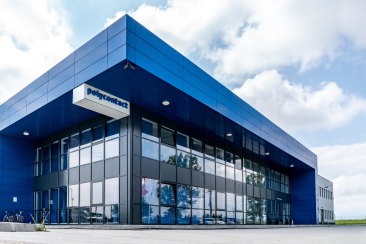 Modernes Firmengebäude von Polycontact mit blauer Metallfassade, grossen Fensterfronten und markantem Eingangsbereich unter leicht bewölktem Himmel.