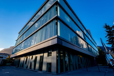 Würth: Modernes Gebäude mit blauer Glasfassade und metallischer Verkleidung, Würth-Schriftzug an der Eingangsfassade, unter klarem Himmel.